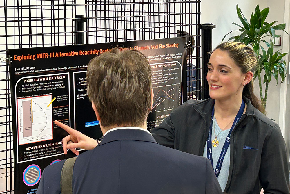Graduate student, Sara Hauptman infront of a poster at a conference speaking to a conference attendee, MIT
