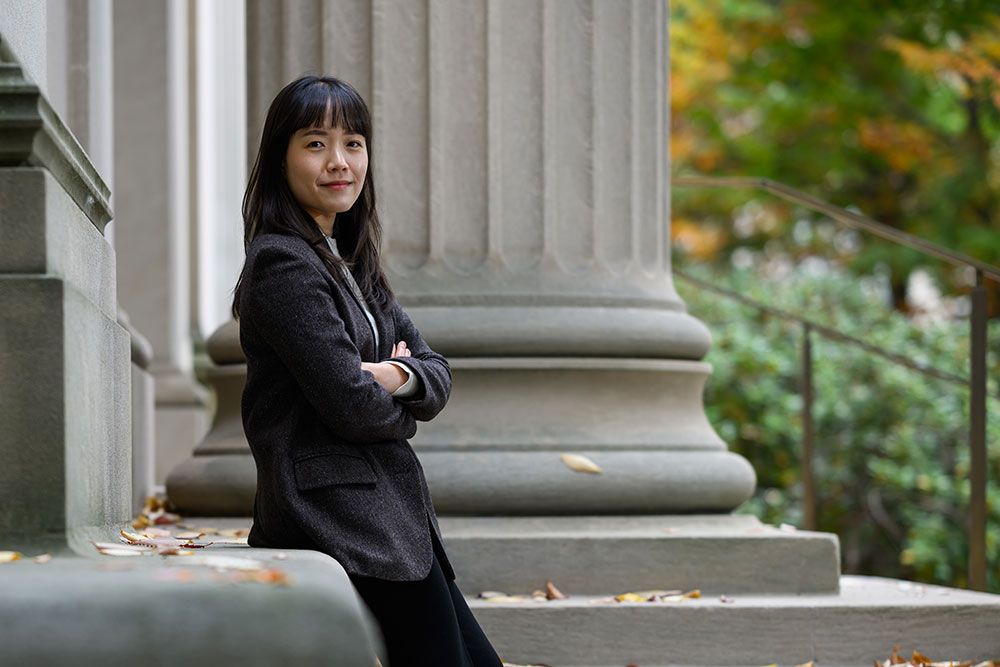 Graduate student Youyeon Choi, arms folded outside on a path with trees on the right.